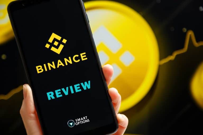 A hand holds a smartphone displaying the words "Análise da Binance Exchange" alongside the Binance logo. In the background, large Binance logos accompany an ascending line graph, signifying growth or analysis.