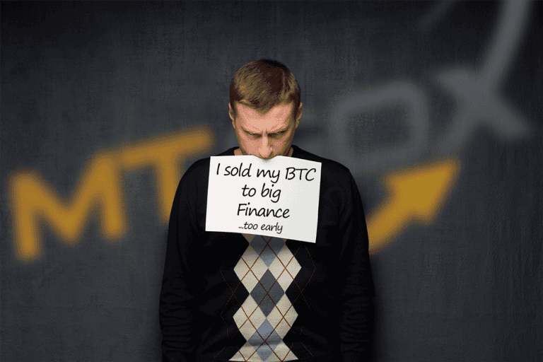 A man wearing a dark sweater with an argyle pattern holds a sign that reads, "I sold my BTC to big Finance ...too early." The background includes partial, blurred text "MT" with a yellow arrow pointing upwards.